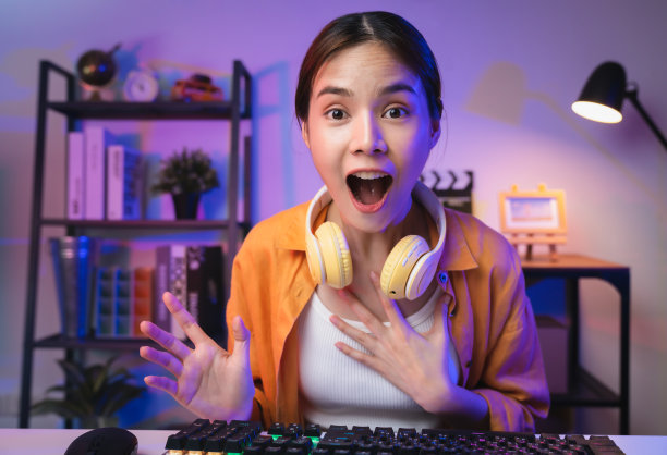 年轻的亚洲女玩家张大嘴巴，带着激动和震惊的表情，戴着耳机庆祝胜利，表达成功。图片下载