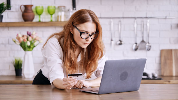 一个女孩站在厨房的笔记本电脑前，手里拿着信用卡图片下载