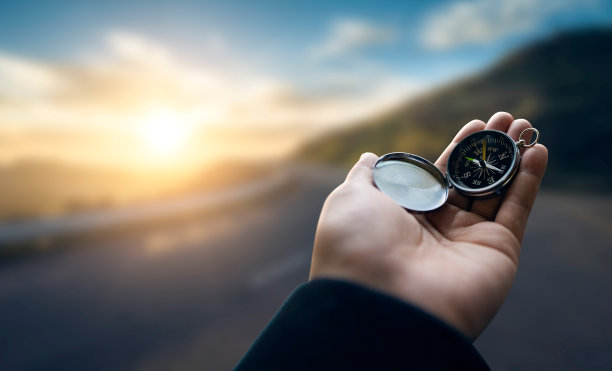 旅行者探险家手里拿着指南针在山间日出，眺望远方。图片下载