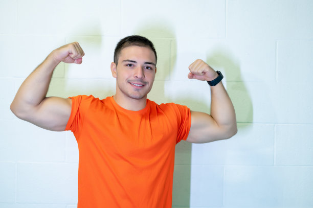 漂亮的照片，年轻的白人男性运动员弯曲他的手臂微笑着看着镜头。自信和积极的成功理念。副本的空间。图片下载