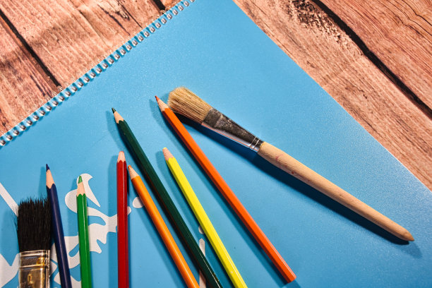 一张木桌上放着蓝色的笔记本和各种颜色的铅笔和刷子图片下载