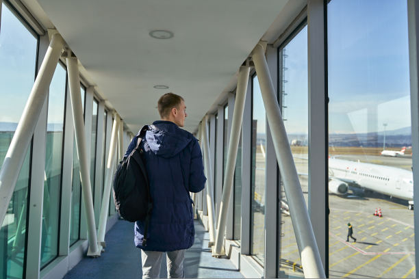 无法辨认的男性旅行者背着背包走在机场的后视图。男子在飞机上登机途中通过航站楼门走廊的后视图。图片下载