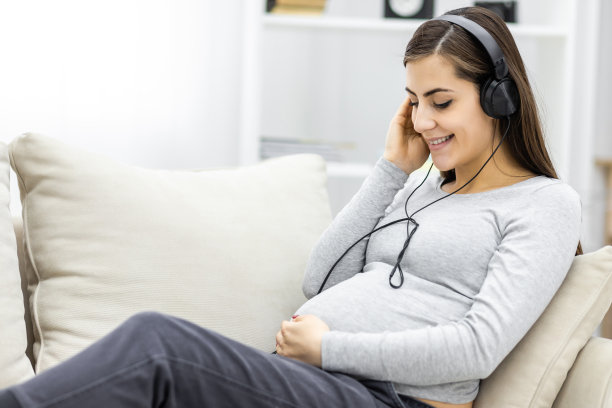 侧面照片的孕妇与耳机在肚子上。图片下载