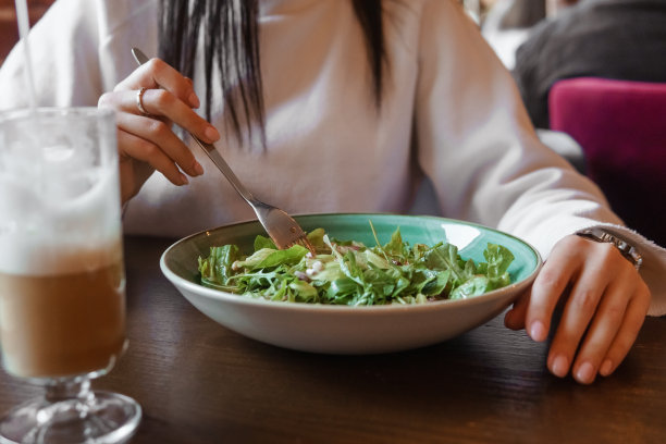 黑发女子正在咖啡馆的桌子前摆弄平板电脑。喝拿铁咖啡，吃植物油。自由职业和自由工作时间表的话题。图片下载