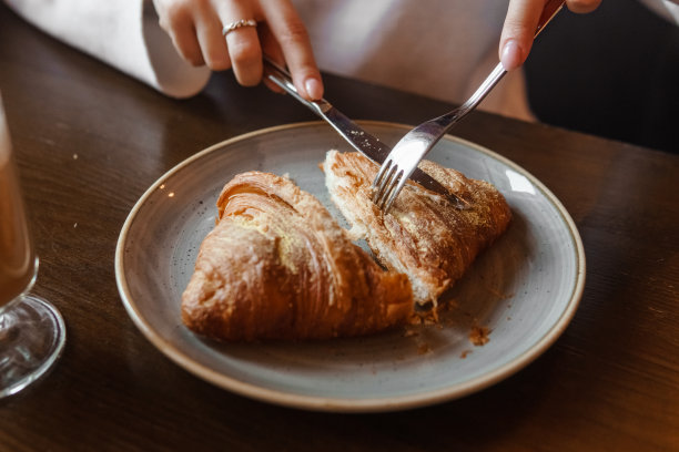 一个女孩在餐厅的木桌上吃羊角面包。在盘子上切羊角面包，特写图片下载