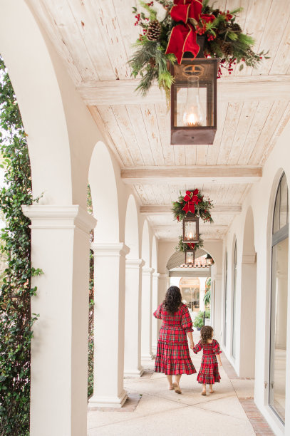 2022年12月，在南佛罗里达州，一位31岁的古巴母亲和她3岁的小女孩走在一起，她有棕色卷发和棕色眼睛，穿着喜庆的红色圣诞格子格纹罩衫裙子，拍摄“快乐与光明”家庭圣诞照片图片下载