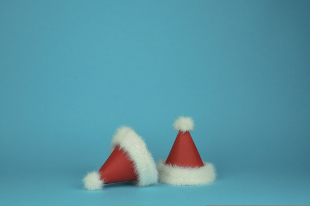 两个圣诞老人的红色和白色羽毛帽子在蓝色的背景。极简风格的卡。图片下载