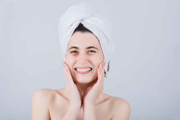 头戴毛巾的年轻女子对着镜头微笑。身体护理概念。年轻女孩在淋浴后用毛巾擦干头发。图片下载
