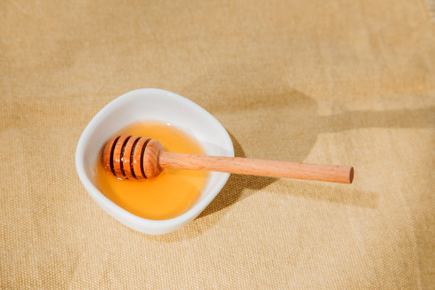 白色的盘子，蜂蜜和木勺放在棕色桌布上图片下载