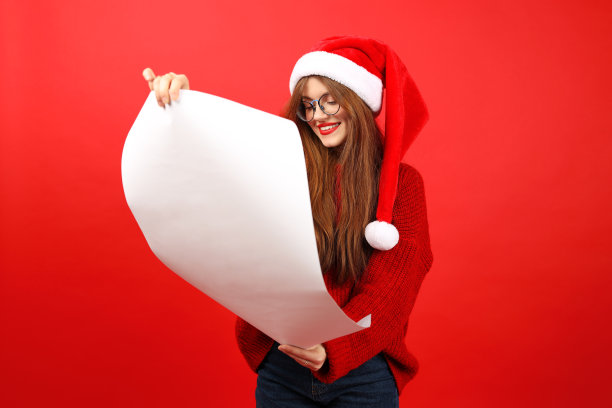 一位戴着红色圣诞帽的年轻女子手里拿着一大堆新年和圣诞节的成就和愿望。图片下载