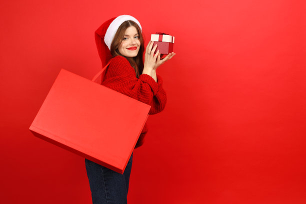 节日折扣和促销。快乐的有吸引力的女人与礼物和红色包装穿着圣诞老人的帽子和毛衣。图片下载