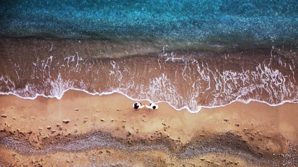 一对年轻人在地中海海岸附近的海滩上手牵着手，这张照片来自无人机，从上面拍摄图片下载