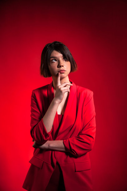 肖像十几岁的黑发女孩穿着时髦的红色西装与潮流的发型在红色背景墙，梦想仰望。年轻美丽的女士陷入了沉思。时尚风格概念。复制文本空格图片下载