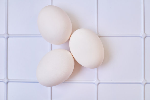 三个鸡鸟蛋放在白色格子塑料表面上。图片下载