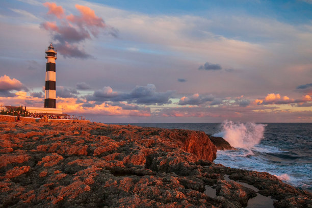 美丽的照片，灯塔在多云的天空和岩石海岸日落图片下载