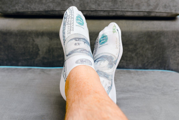 一个男人光着脚躺在床上，袜子上印着一美元的图案。室内拍摄，选择性对焦，特写。图片下载