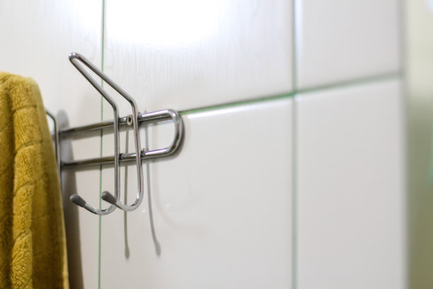 离焦芥末毛巾挂在钩子上。浴室瓷砖墙的金属粘毛巾衣架。浴室架子上挂着的芥末毛巾特写。副本的空间。焦点不清图片下载