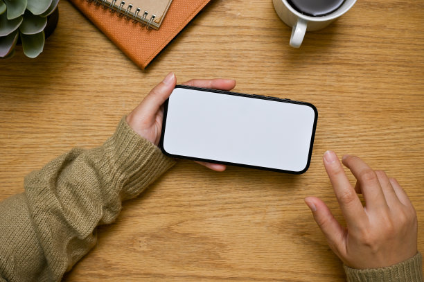 一位女士的手里拿着一个水平摆放的智能手机模型，放在木桌上。图片下载