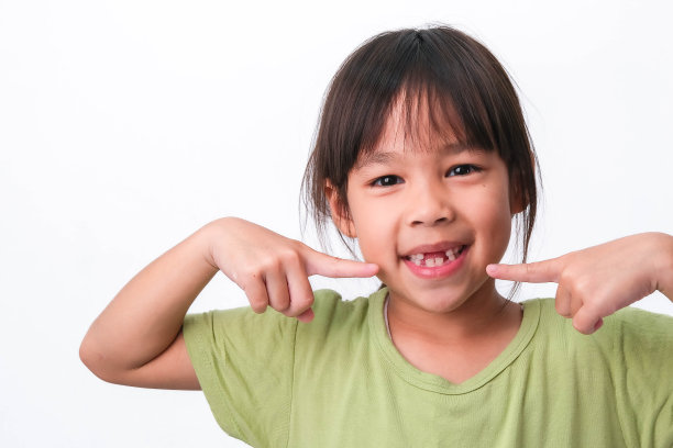 一个亚洲女孩的肖像破碎的乳牙和第一恒牙。友好的小女孩在白色背景上展示她破碎的牙齿。图片下载