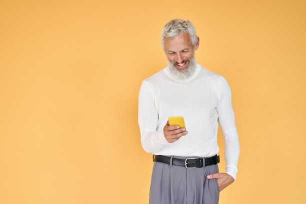 快乐的老商人用手机站在孤立的黄色上。图片下载