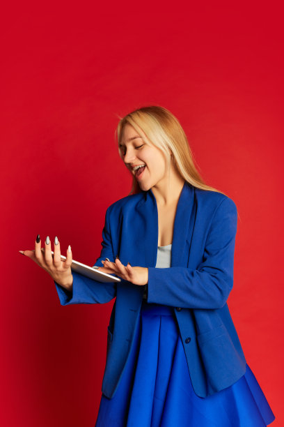 积极的年轻女商人或快乐的学生穿着蓝色西装摆姿势在明亮的红色背景。创业、动力、事业、情感、成就概念图片下载