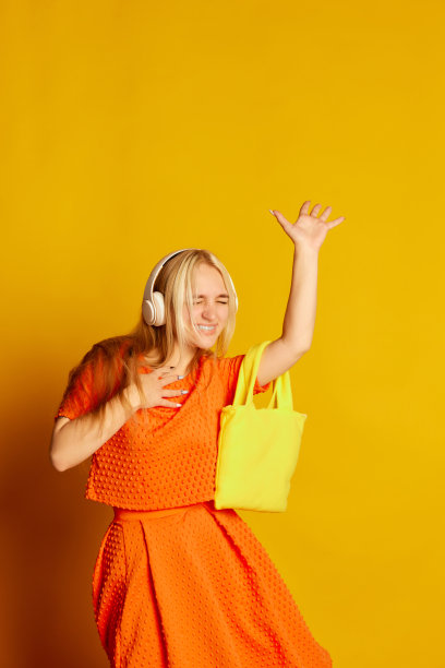 跳舞的年轻美丽的情感女孩在橙色的裙子跳舞，微笑，有乐趣孤立在橙色的背景。生动的情感，快乐，爱好和快乐图片下载