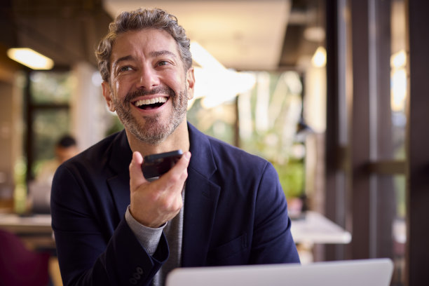 成熟的商人在办公桌上的笔记本电脑上工作，对着手机的麦克风说话图片下载