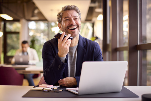 成熟的商人在办公桌上的笔记本电脑上工作，对着手机的麦克风说话图片下载