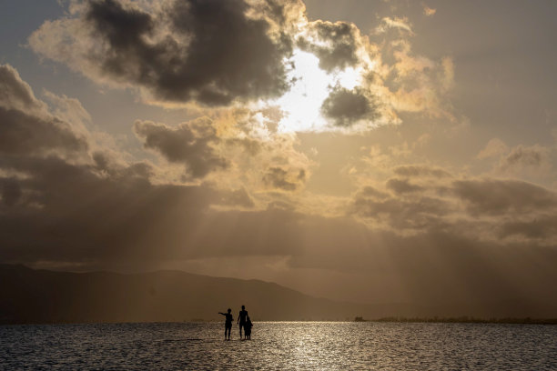 落日时分，三个人的剪影出现在海上的冲浪板上图片下载