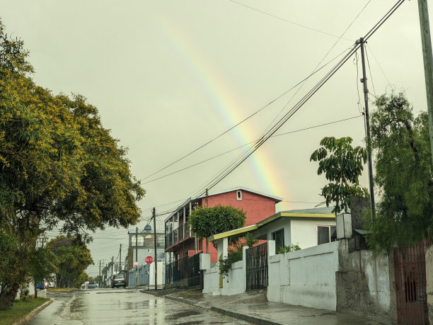 雨后乌云密布的天空中，城市街道和建筑物上出现了鲜艳的彩虹图片下载