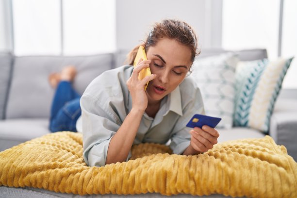 年轻女子拿着信用卡在家里用智能手机说话图片下载