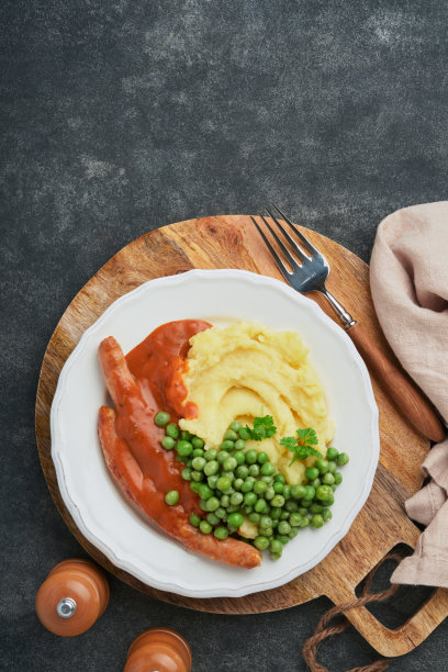 香肠和马铃薯泥。烤香肠配土豆泥和绿豌豆，白色盘子，黑色背景。大不列颠和爱尔兰的传统菜肴。烧烤牛肉香肠。前视图。图片下载