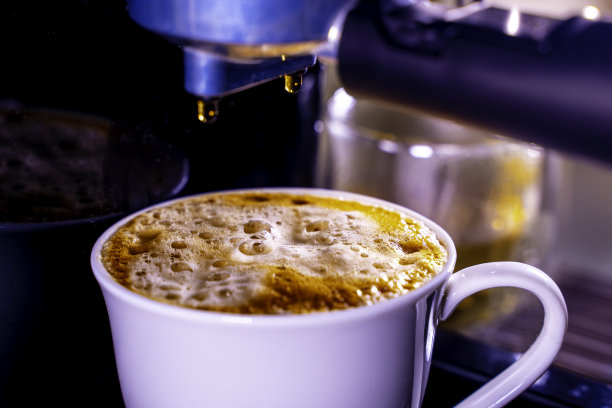 咖啡泡沫特写。浓缩咖啡从全自动咖啡机里出来，把咖啡机变成杯子。软的焦点。图片下载