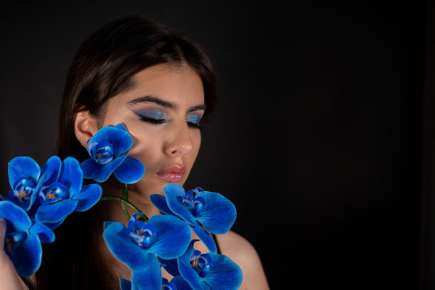 迷人的冷静放松的黑发女人与完美的皮肤，闭上眼睛与蓝色的眼罩，蓝色的花图片下载