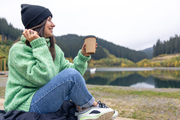一个年轻的女人端着一杯咖啡，背景是模糊的山脉。图片下载