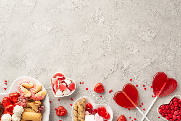 情人节的概念。顶部视图照片的心形盘子与糖果巧克力果冻糖果饼干棒棒糖和五彩纸屑混凝土纹理背景与空白图片下载