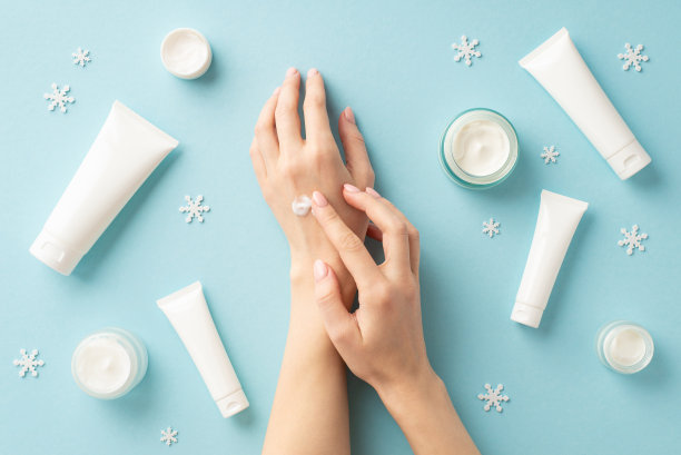 冬季护肤产品概念。第一人称俯视图照片的女孩应用在她的手罐子管没有标签和雪花孤立的浅蓝色背景与复制空间图片下载