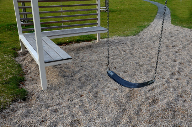 方形大门或框架形状的巨大钢架梁，中间是一根金属杆，上面是供儿童使用的秋千。公园小路旁的草坪。图片下载