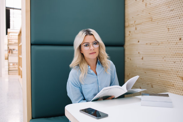 聪明的女性肖像，戴着眼镜保护眼睛，在舒适的大学图书馆里花时间从事文学爱好，坐在有趣的书旁，看着相机图片下载