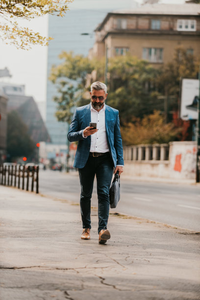 一位西装革履、戴着墨镜的商人背着包在城市里走来走去图片下载