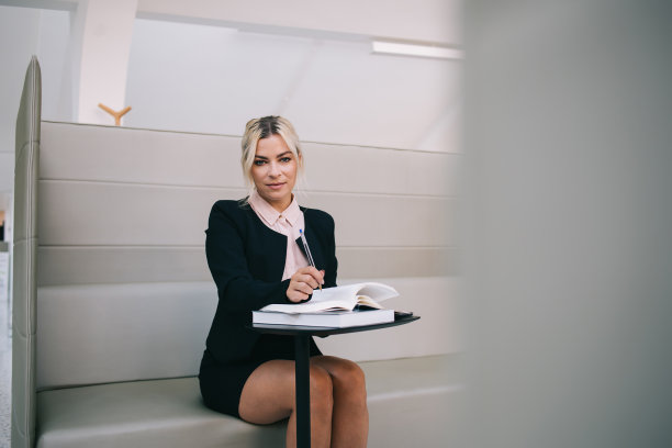 穿着正式的女员工在现代办公室内部工作的肖像，坐在桌子旁，有教育文献，30岁的迷人女人摆姿势，花时间规划创业图片下载