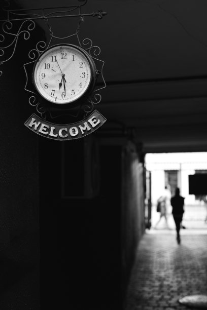 一个男人的剪影在一个旧院子的黑暗走廊里，墙上挂着一个钟。钟上的铭文——欢迎。图片下载