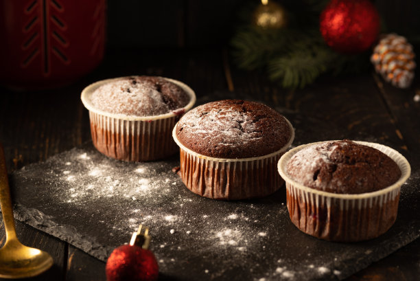 黑色背景上有糖粉的巧克力松饼。圣诞装饰。静物特写。食物的照片。图片下载