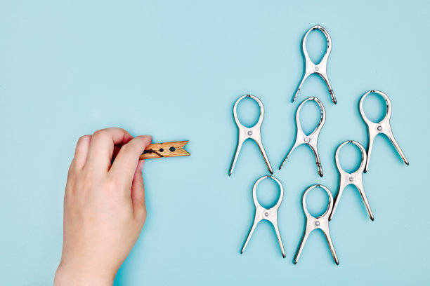 一只手拿着一个木制的晒衣夹，旁边是蓝色桌面上的许多金属晒衣夹图片下载