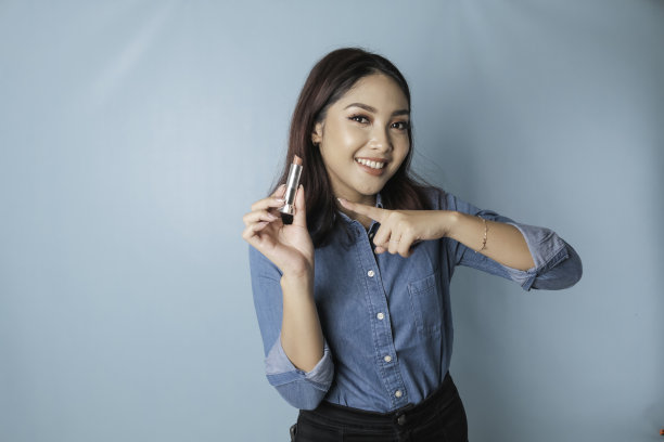 一位年轻美丽的亚洲女性在嘴唇上涂口红的肖像，被蓝色背景隔开图片下载