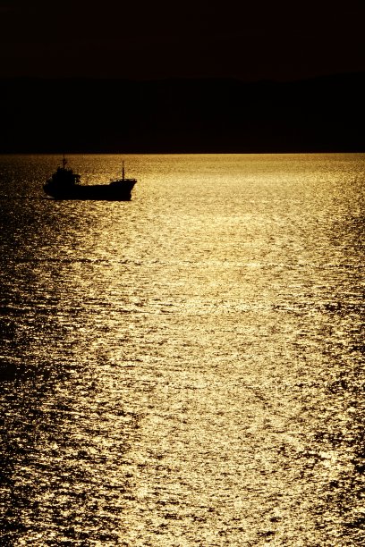 一个明亮的暗青铜日落在海上，上面有工业船和帆船。海参崴海上的日落。海上的日落进入了群山。图片下载