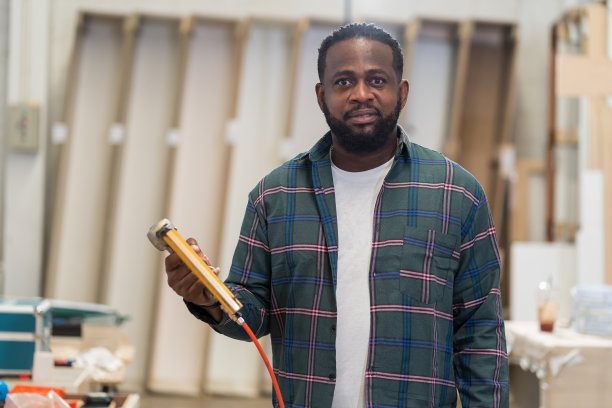 非裔美国木匠持有气动钉枪在木材车间。木工男工人肖像在安全制服和设备工具与气动钉枪工作在木材工厂图片下载