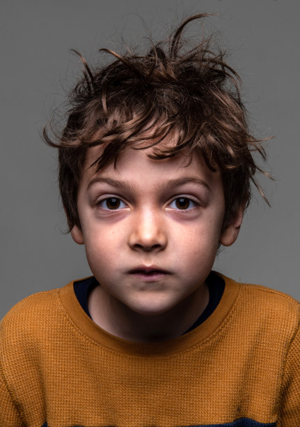 严肃的蓬头垢面的小男孩看着灰色背景上的相机图片下载