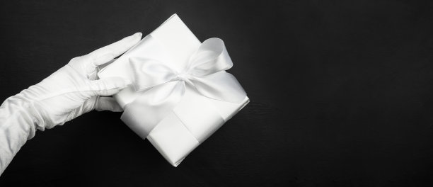 礼盒在手，用白纸包装，黑色背景上有蝴蝶结。节日的概念。圣诞节。“黑色星期五”。情人节。图片下载