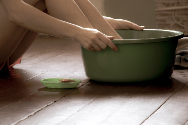 一个女孩在家里的木地板上用绿色盆用水洗脚，足部护理，在家洗脚，卫生，游泳图片下载